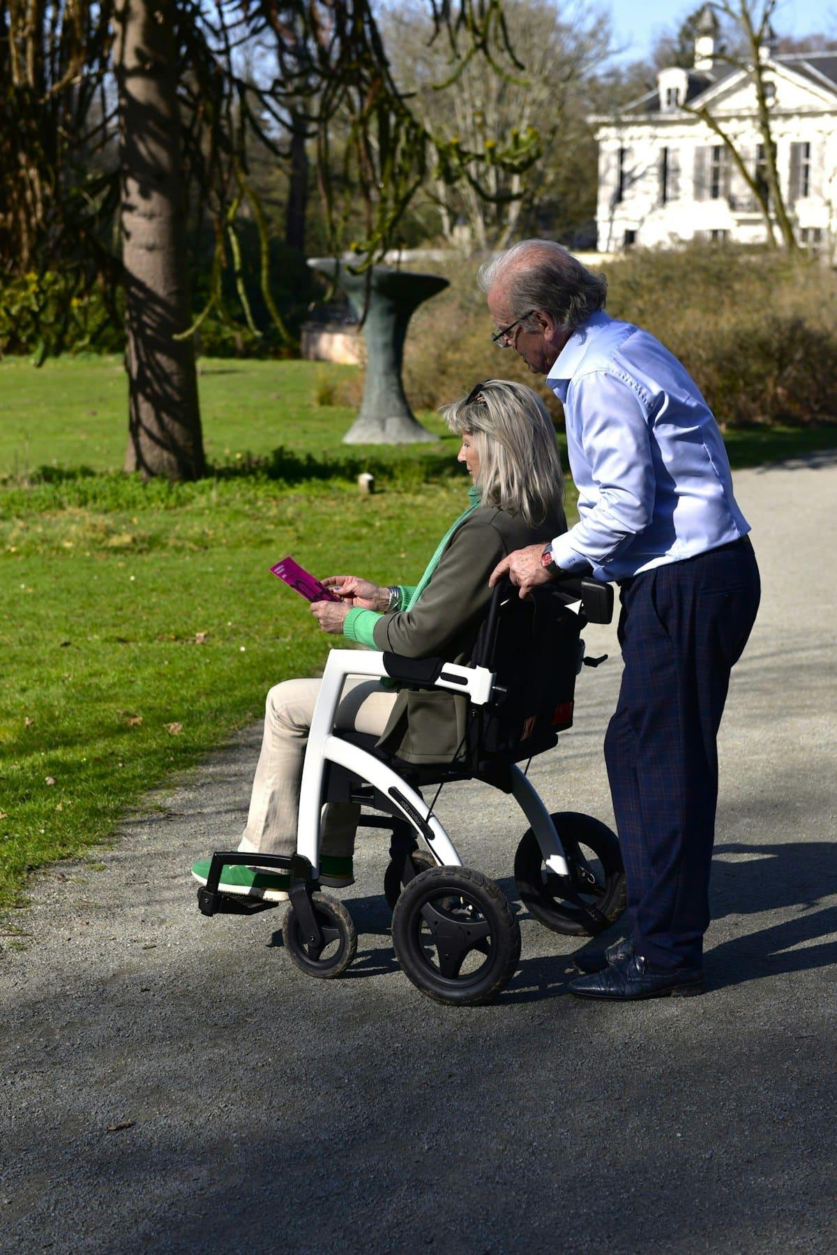 A man helping a woman in a wheelchair through a park