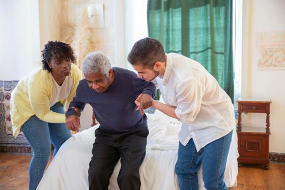 Two support workers helping an older man stand from his chair