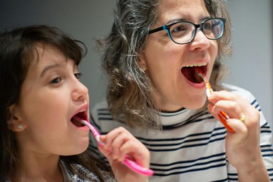 A support worker and a child brushing their teeth together at a bathroom mirror