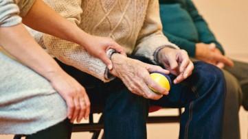 A support worker gently holding the arm of an older man holding a stress ball